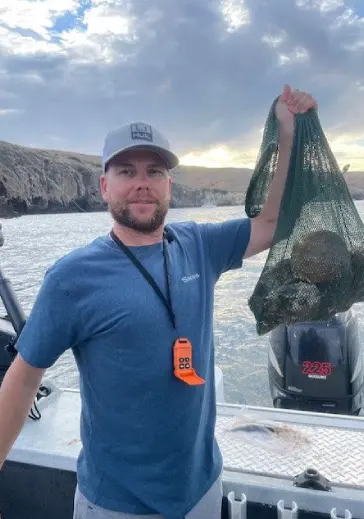 A man holding up a bag of fish on the water.